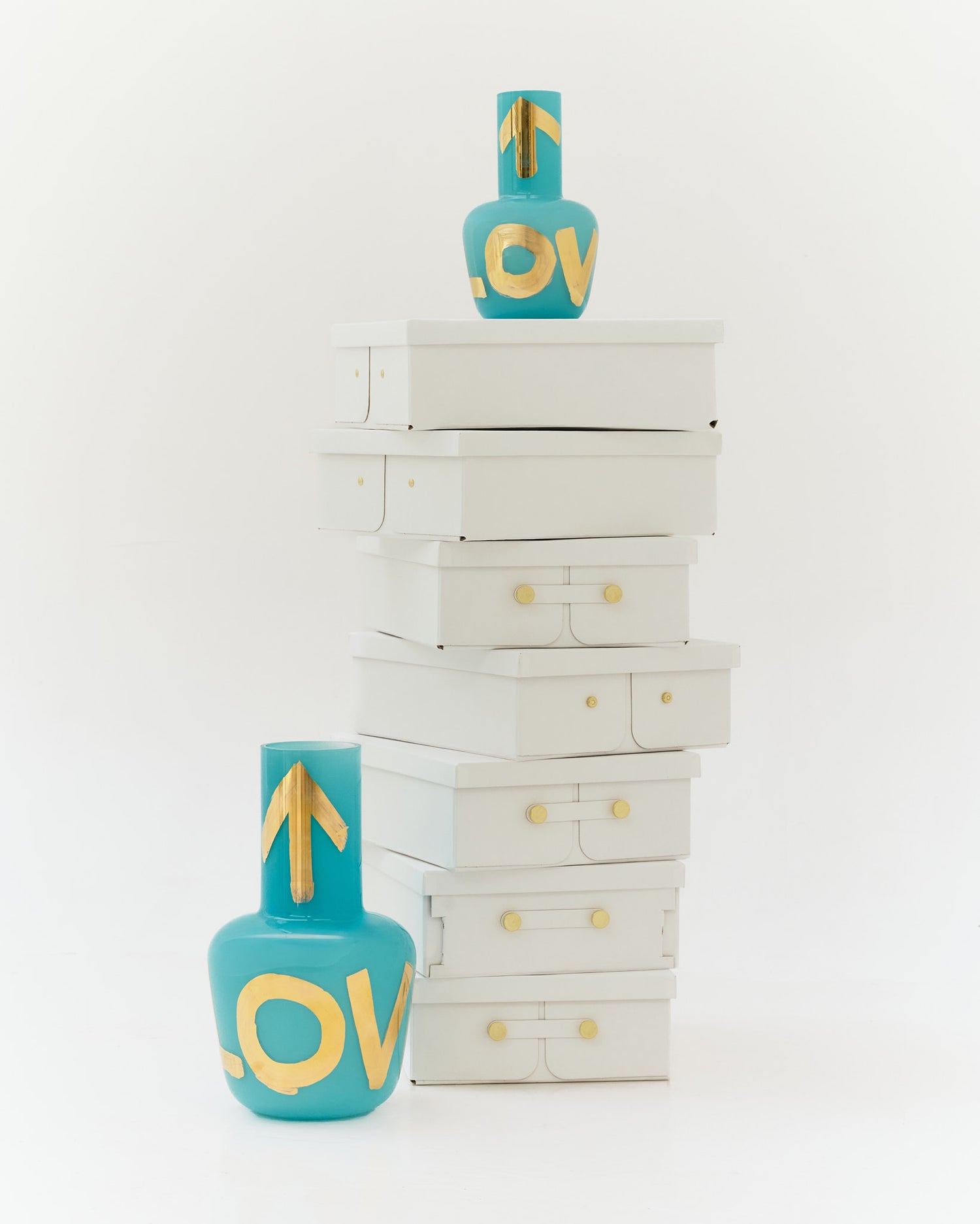 Minimalistic turquoise vase with golden "LOVE" on stacked white boxes, part of Artisème x QUBUS collection.