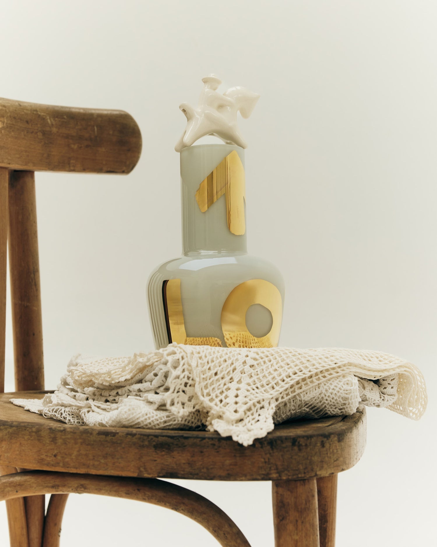 Unnamed Baby váza in šedomodrá on a wooden chair, showcasing elegant design with gold accents and a decorative star.